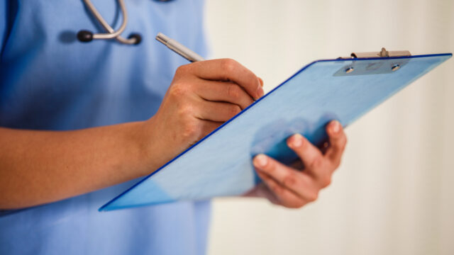 Midsection of unrecognisable nurse holding a medical chart and writing diagnosis in it.