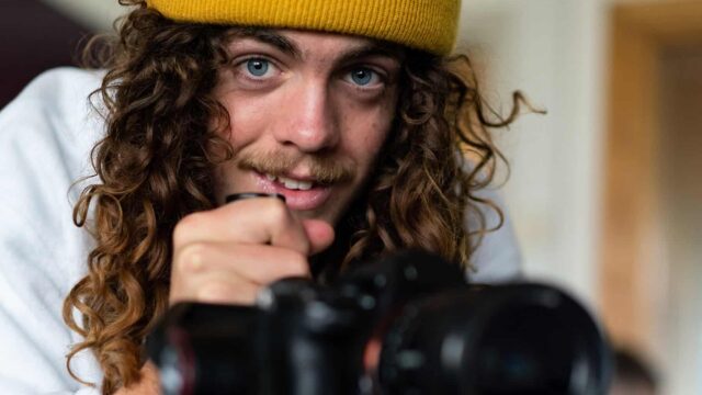 A student looks up from a camera wearing a yellow beanie.