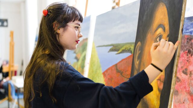 A student painting a large portrait of a woman.