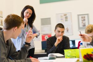 A tutor stands over students who are talking in a classroom.