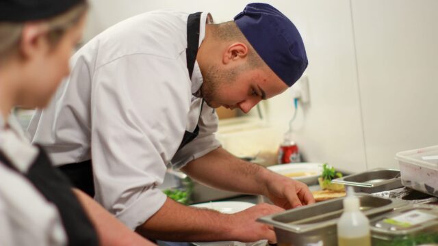 A chef placing food on a plate in a professional kitchen.