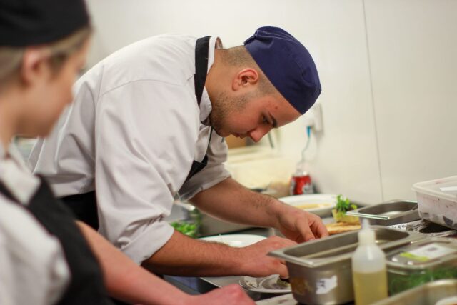 A chef placing food on a plate in a professional kitchen.