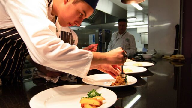 A chef dishing up large white plates with food.