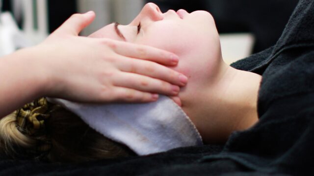 A close up of hands on the side of a woman's face who is lying horizontal.