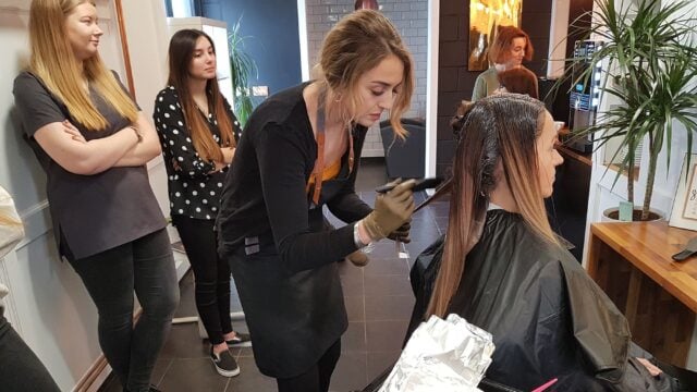 A hairdresser dying a client's hair with observers.