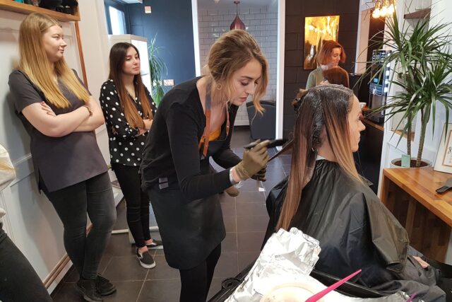 A hairdresser dying a client's hair with observers.
