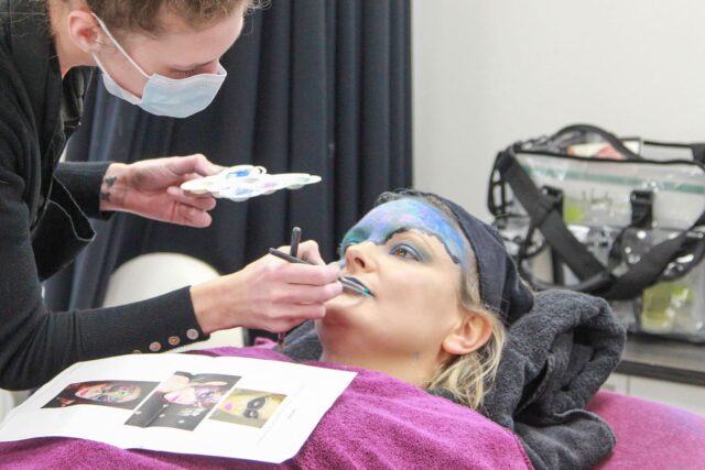 A student putting creative make up on a model.