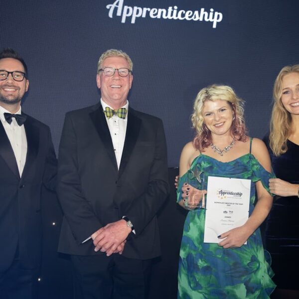 A group of people stood together at the Cornwall Apprenticeship Awards. One person holds up a certificate and a trophy.