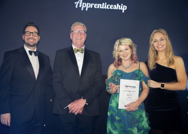 A group of people stood together at the Cornwall Apprenticeship Awards. One person holds up a certificate and a trophy.