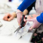 A close up of hands cutting fabric on a table.