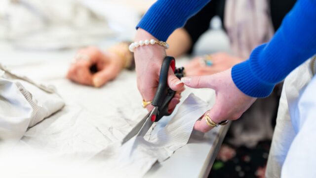 A close up of hands cutting fabric on a table.