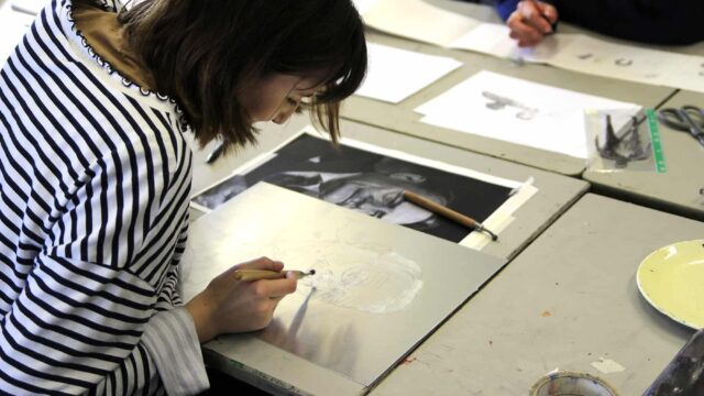 A student leaning over her artwork of a man's portrait.