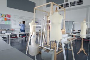 A selection of mannequins in the centre of a classroom while a tutor writes on a whiteboard.