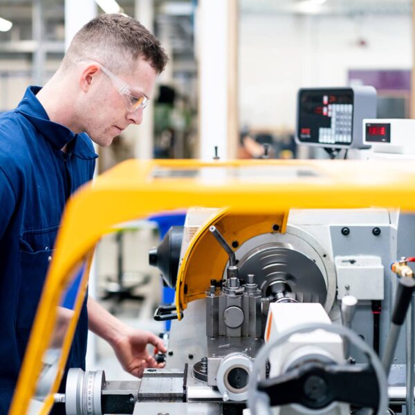 A man in overalls and safety glasses using engineering equipment.