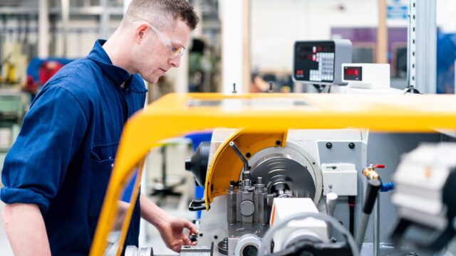 A man in overalls and safety glasses using engineering equipment.