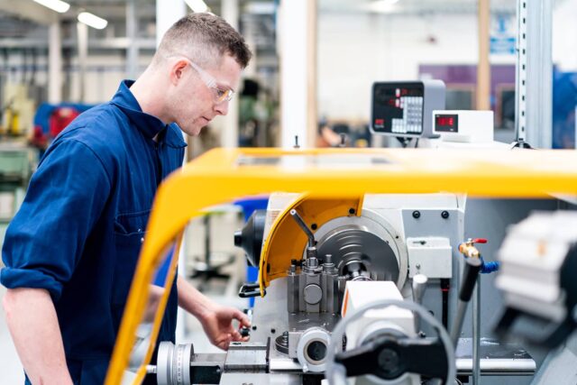 A man in overalls and safety glasses using engineering equipment.