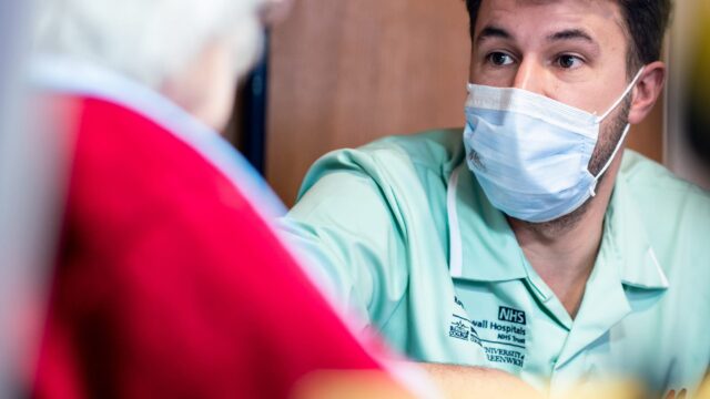 A care worker wearing a mask looks to an elderly unrecognisable person.