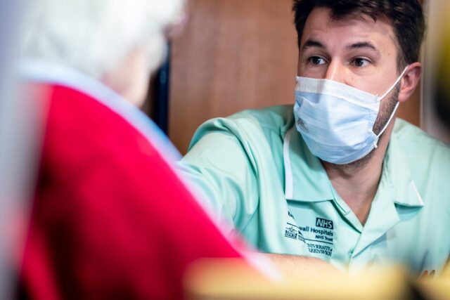 A care worker wearing a mask looks to an elderly unrecognisable person.