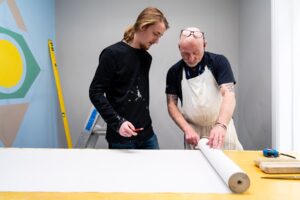 A tutor and a student look at a roll of wallpaper together.