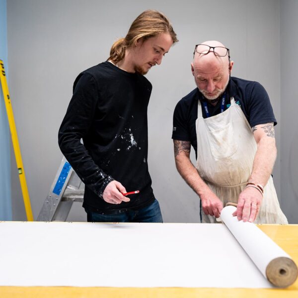 A tutor and a student look at a roll of wallpaper together.