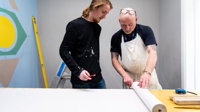 A tutor and a student look at a roll of wallpaper together.