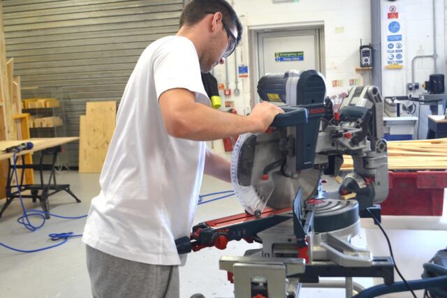 A student uses a saw whilst wearing protective equipment.