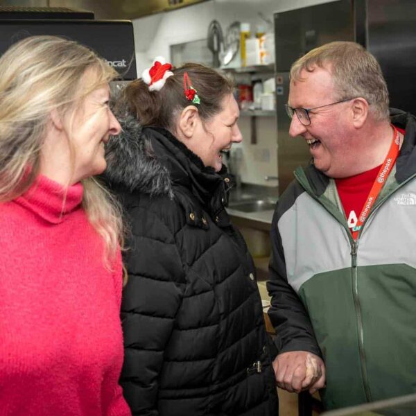 A man holds the hand of a woman and they are laughing. Another woman looks at them smiling.