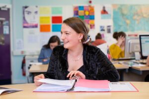 A student looks through a ring binder folder at a classroom table.