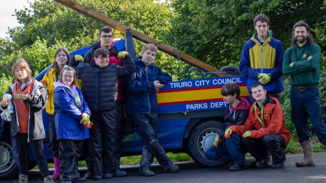 A group of students stand in front of a vehicle that says 'Truro City Council Parks Dept' on the side.