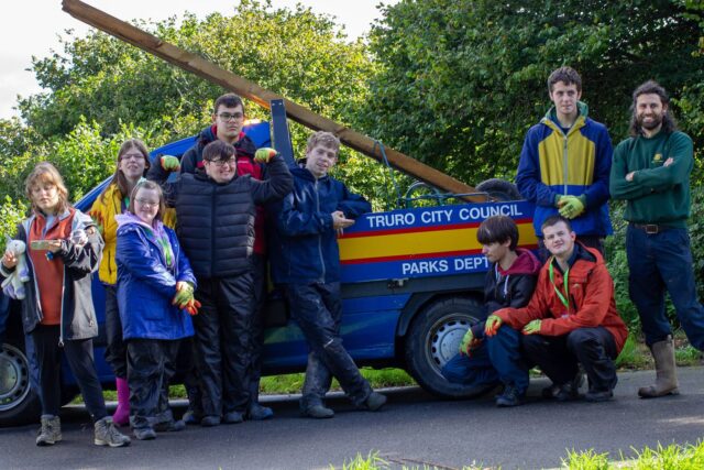 A group of students stand in front of a vehicle that says 'Truro City Council Parks Dept' on the side.