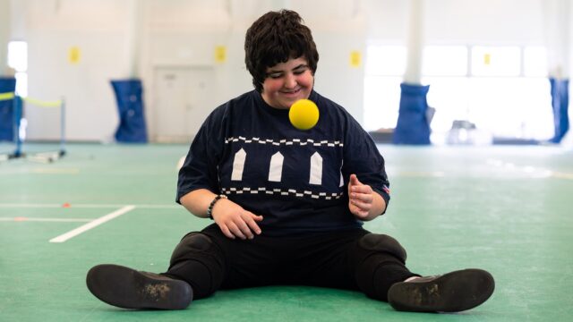 A student sits on the ground and bounces a yellow ball.