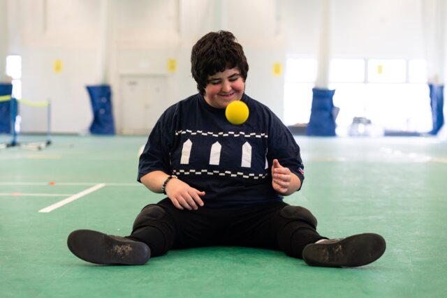 A student sits on the ground and bounces a yellow ball.