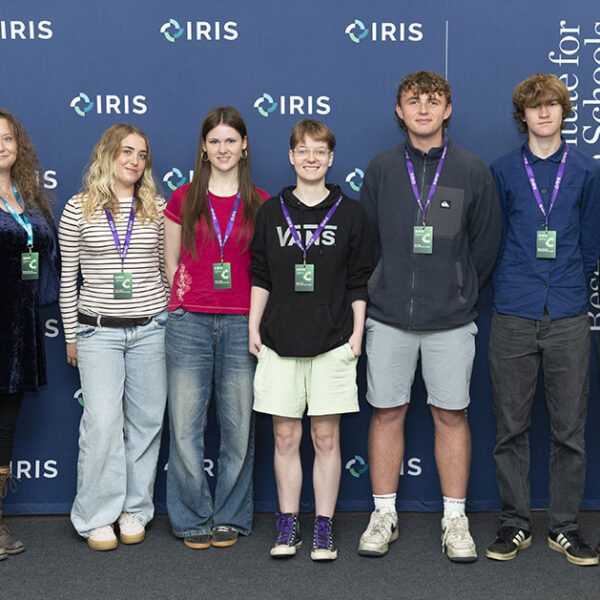A group shot of students stood in front of banners. They are all wearing visitor lanyards.