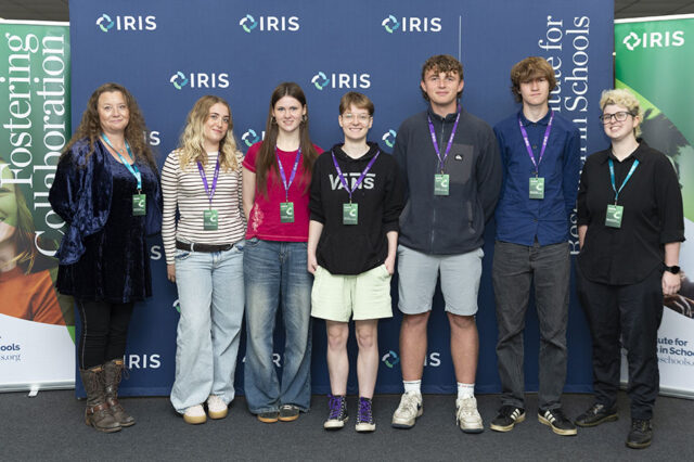 A group shot of students stood in front of banners. They are all wearing visitor lanyards.