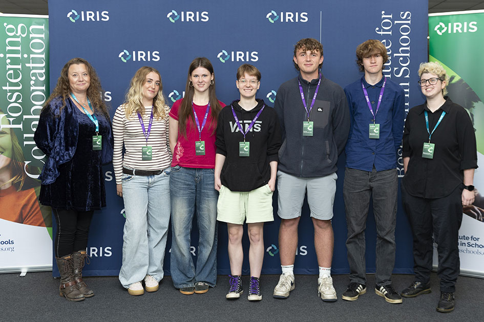 A group shot of students stood in front of banners. They are all wearing visitor lanyards.