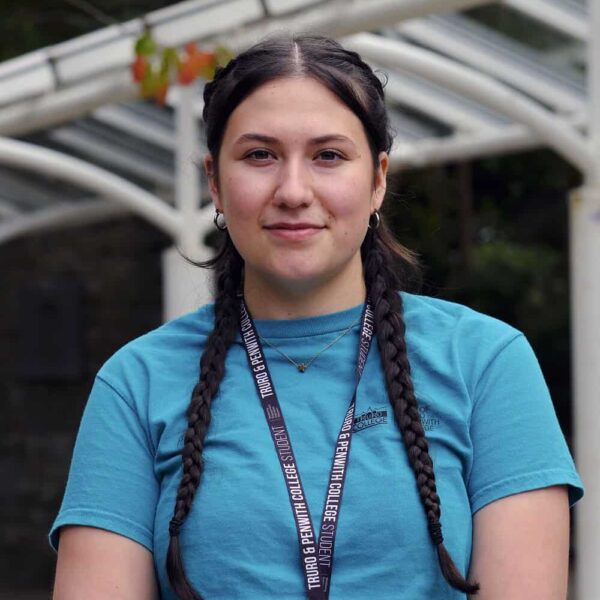 A student with plaits is wearing a blue ambassador T shirt and student lanyard.