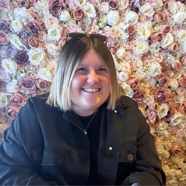 A woman wearing black with a flower display behind her.