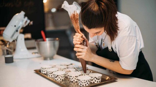 A chef pipes chocolate into small cases on a baking tray.