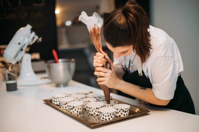 A chef pipes chocolate into small cases on a baking tray.