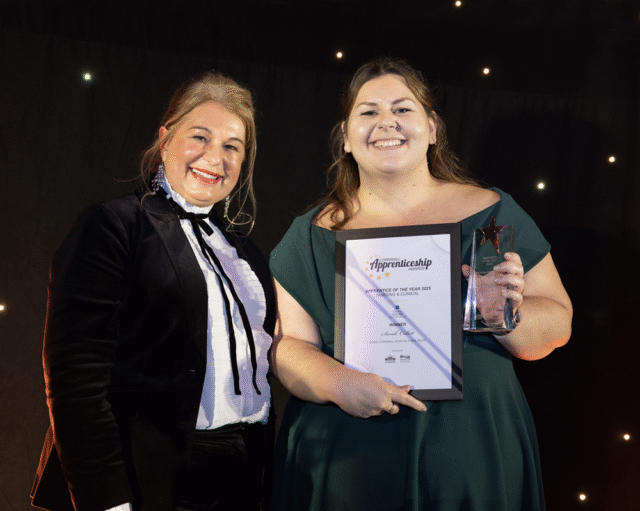 Sarah holds her trophy and certificate and is accompanied by another woman.