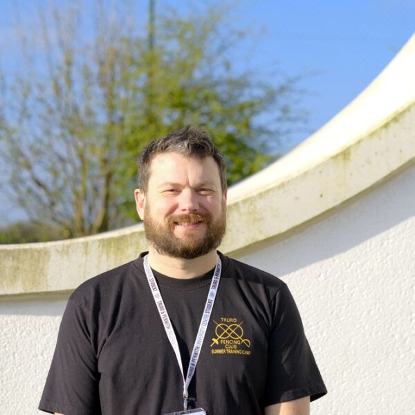 Simon is stood outside in the sun wearing a lanyard.