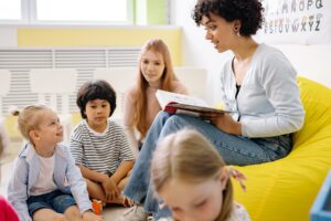 A teacher reads a story to young children on a bean bag.