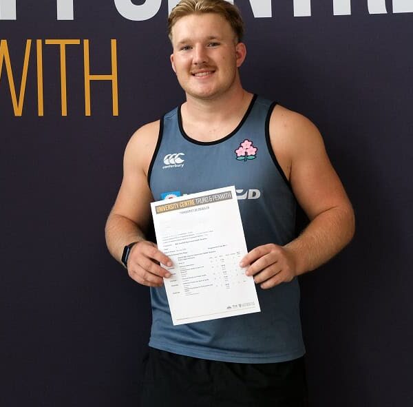 Lachlan stands in front of a dark backdrop and holds up a copy of his results.