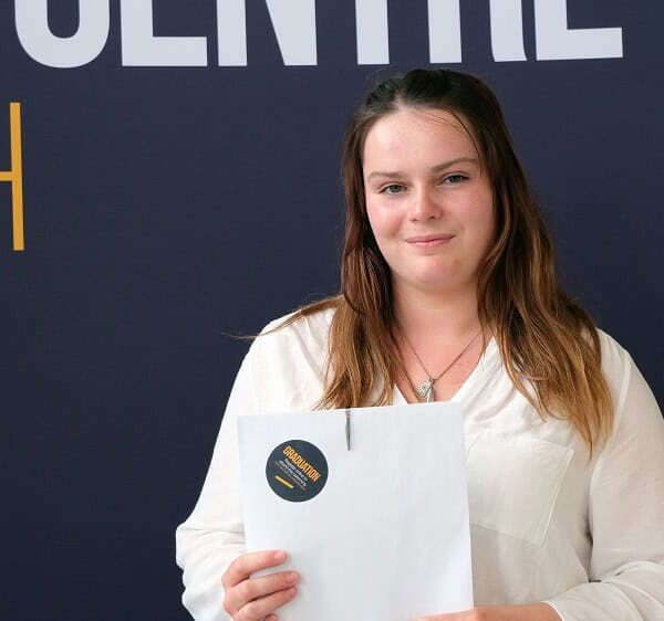Caley holds up her results in front of a dark backdrop.