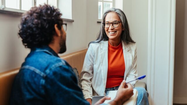 Two coworkers engaging in a creative conversation while seated in an office lounge area, fostering a collaborative work environment.