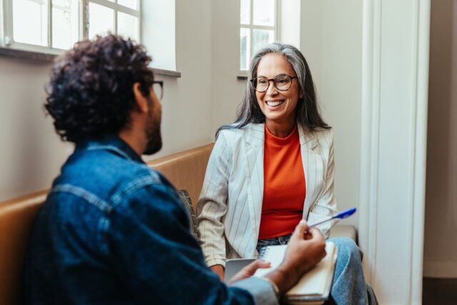 Two coworkers engaging in a creative conversation while seated in an office lounge area, fostering a collaborative work environment.