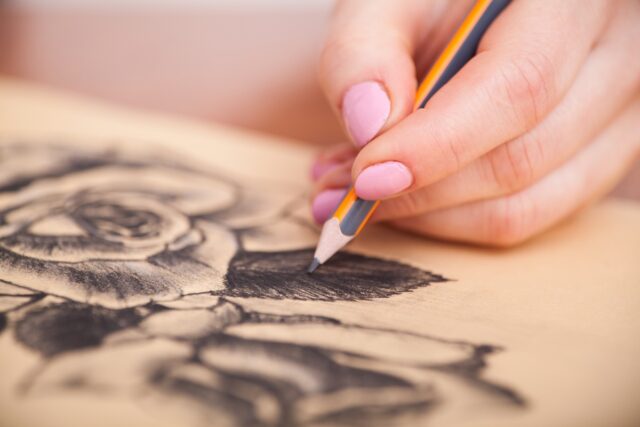 Closeup of woman's hands with a pencil drawing beautiful bunch of roses at the desk