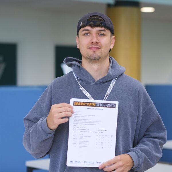 A photo of Jaydon. He is wearing a blue hoodie and a lanyard and is holding his results in front of him.