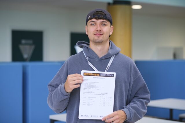 A photo of Jaydon. He is wearing a blue hoodie and a lanyard and is holding his results in front of him.