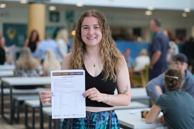 A photo of Lauren, she is holding her results up and she is wearing a black vest top. She has long blonde hair.